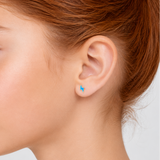 Close-up of a person wearing a small blue lightning bolt earring on a plain background